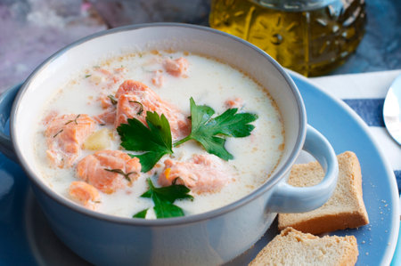 Creamy salmon soup Kalakeitto with salmon, carrot, parsley, onion, garlic, potatoes, croutons and spoon in blue bowl. Traditional Finnish hot soupの写真素材