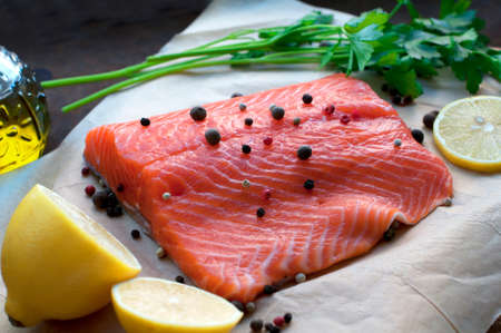 Trout fillet with lemon, parsley, allspice, olive oil on parchment paper on dark brown backgroundの写真素材
