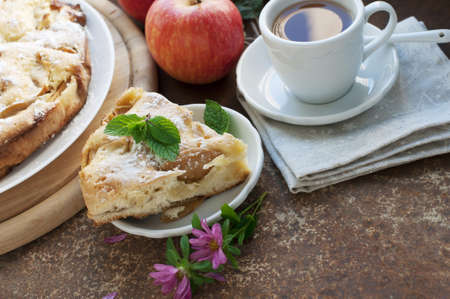 Apple homemade pie with red apples, mint and cup of tea, flowers on dark brown background. Rustic styleの写真素材