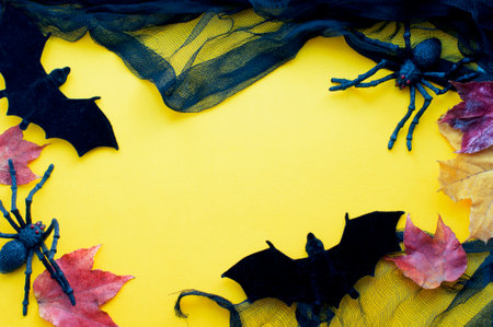 Halloween yellow background with bats and black spiders with autumn leaves. Halloween decorations on yellow background. Top viewの写真素材