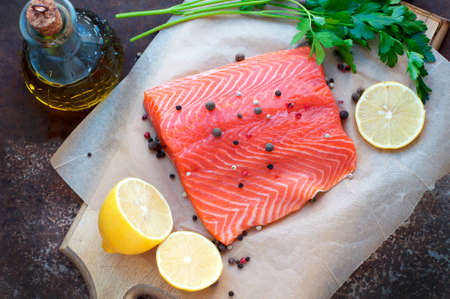 Trout fillet with lemon, parsley, allspice, olive oil on parchment paper on dark brown background. Top viewの写真素材
