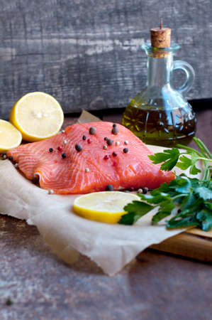 Trout fillet with lemon, parsley, allspice, olive oil on parchment paper on dark brown backgroundの写真素材