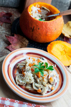 Baked pumpkin stuffed rice, carrots, pepper and mushrooms with parsley on brown plate on dark brown background. Healthy vegetarian foodの写真素材