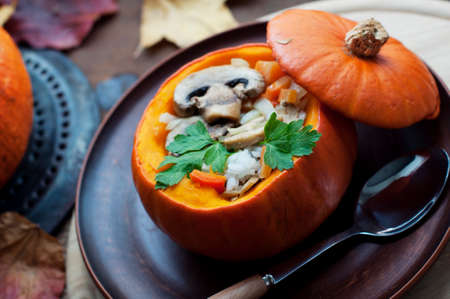 Baked pumpkin stuffed rice, carrots, pepper and mushrooms with parsley on brown plate on dark brown background. Healthy vegetarian foodの写真素材
