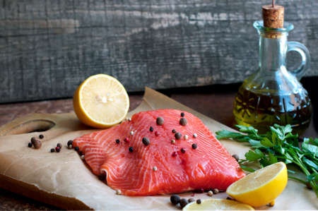 Trout fillet with lemon, parsley, allspice, olive oil on parchment paper on dark brown and wooden backgroundの写真素材
