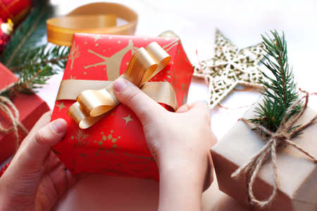 Children's hands packing a box with gifts. Boxes with gifts in red, gold and beige paper with ribbons, beads, star, fir branch. Christmas gifts with New Year's decor on a white background.の写真素材