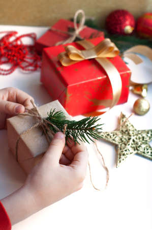 Children's hands packing a box with gifts. Boxes with gifts in red, gold and beige paper with ribbons, beads, star, fir branch. Christmas gifts with New Year's decor on a white background.の写真素材