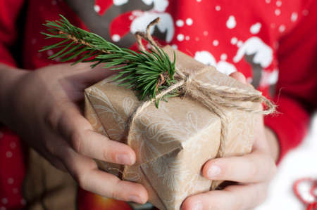 Children's hands packing a box with gifts. Boxes with gifts in red, gold and beige paper with ribbons, beads, star, fir branch. Christmas gifts with New Year's decor in handの写真素材