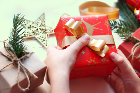 Female hands wrapping Christmas gifts in red paper with golden ribbon.の写真素材