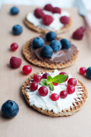 Waffles with cream cheese, cranberries and raspberries on a wooden board on a pink background. Romantic breakfast with fruits on waffles and white laceの写真素材