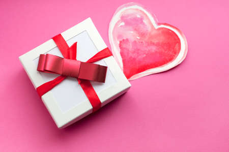 White box with gift, watercolor heart and red bow on pink background. Valentine's day gift. top view. Space for textの写真素材