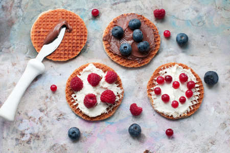 Waffles with cream cheese and chocolate, cranberries, raspberries and blueberries on a gray background. Romantic breakfast with knife, fruits on waffles. top viewの写真素材