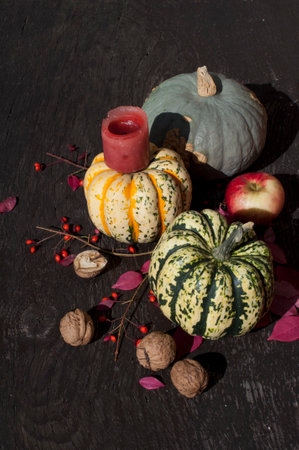 Multicolored pumpkins with walnuts, an apple, a red candle and autumn leaves on a wooden background. Autumn harvest of pumpkinsの写真素材