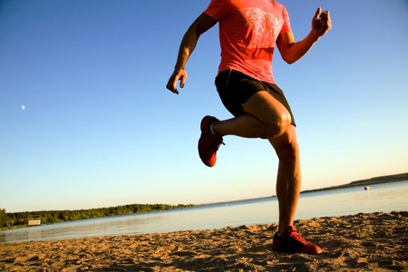 Young man running along the seashore at sunset.の写真素材