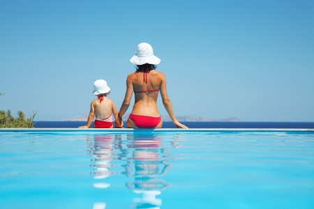 Young mother with baby daughter sitting on the edge of the pool and stare at the seaの写真素材
