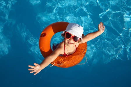Funny little girl swims in a pool in an orange life preserverの写真素材