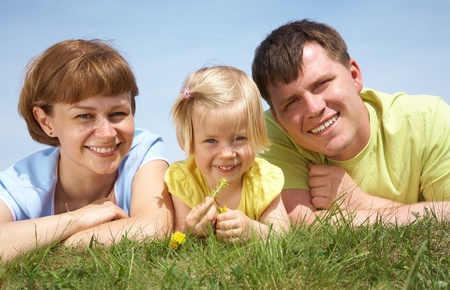 family lifestyle portrait of a mum and dad with their daughter having good time on the green grassの写真素材