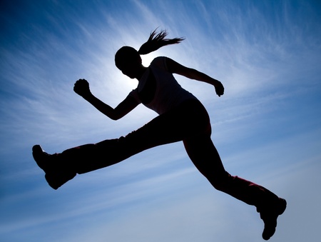 Female runner silhouette against the blue sky and sunの写真素材