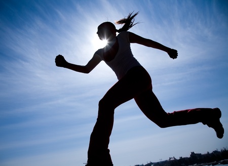 Female runner silhouette against the blue sky and sunの写真素材