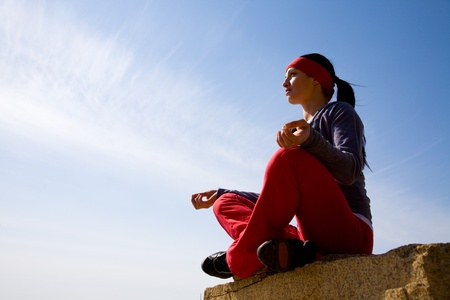 The beautiful girl is engaged in yoga on the rock against the blue の写真素材