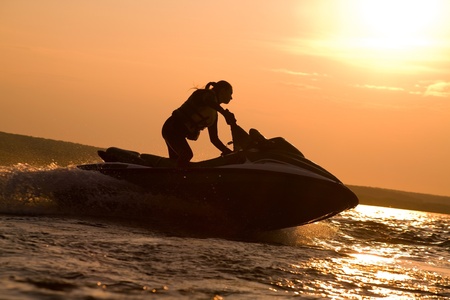 beautiful girl riding her jet skis in the sea at sunset .spray