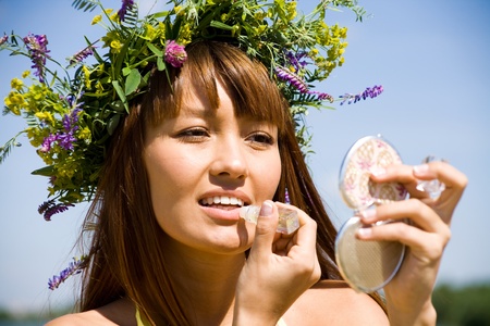 Portrait of Young beautiful woman in floral wreath uses lipstickの写真素材