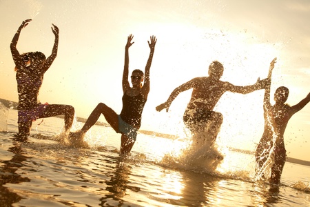 group of happy young people dancing and spraying at the beach on beautiful summer sunset の写真素材