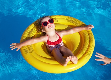 Funny little girl swims in a pool in an yellow life preserverの写真素材