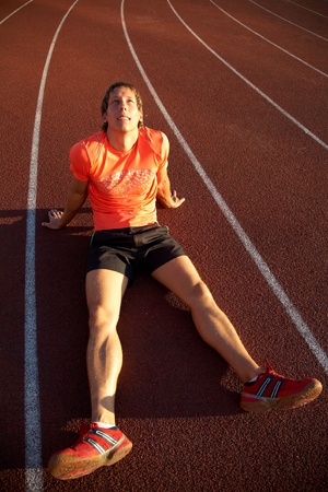 young athlete sits on the treadmill stadium legs spread. Failure.