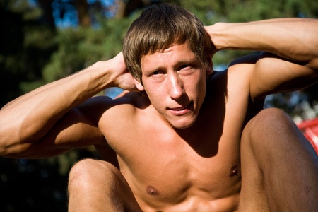  young handsome man performs sport exercises to strengthen muscles outdoorsの写真素材