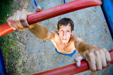 young handsome man performs sport exercises to strengthen muscles outdoors