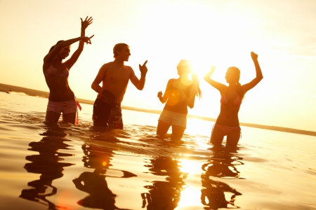 group of happy young people dancing and spraying at the beach on  beautiful summer sunsetの写真素材