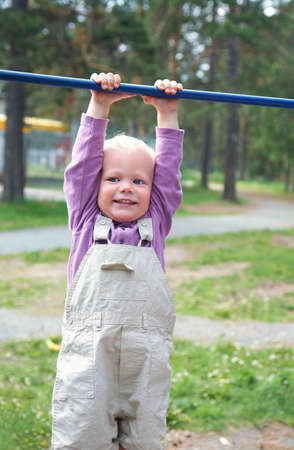 Portrait of little boy hang on horizontal bar in summer park