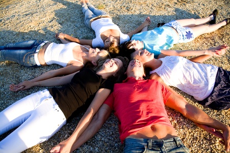 group of young people lie on the beach holding hands enjoying relaxの写真素材