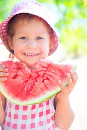 little girl eating a ripe juicy watermelon in summertimeの写真素材