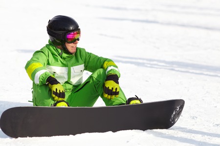 young snowboarder sitting on snow and smilingの写真素材