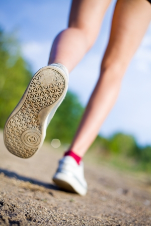 female legs in sneakers are running on a background of roadの写真素材