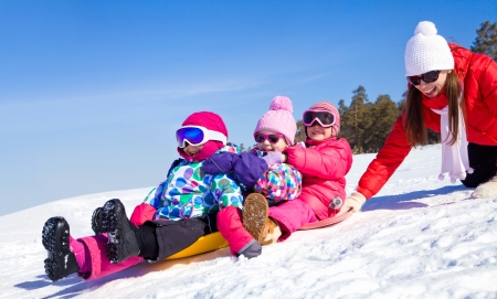 Young mother with  children riding with snow slides in winter time