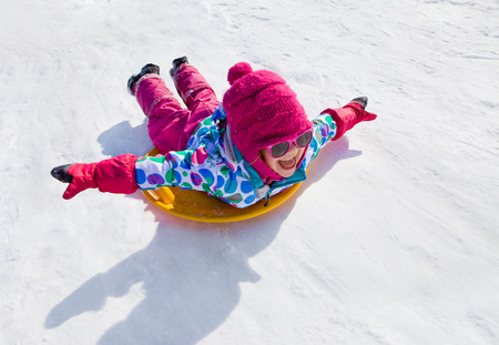 little girl riding on snow slides in winter timeの写真素材