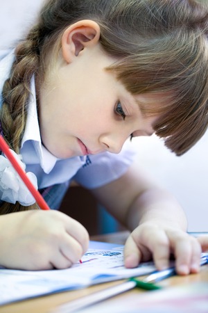 schoolgirl with pen writing in a notebook in classroomの写真素材