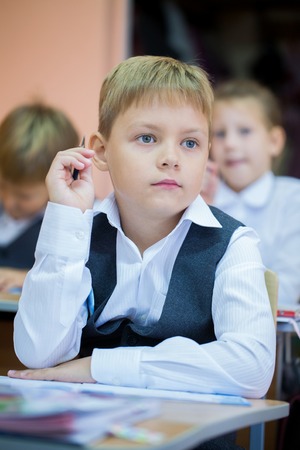 little schoolboy with pen in classroomの写真素材