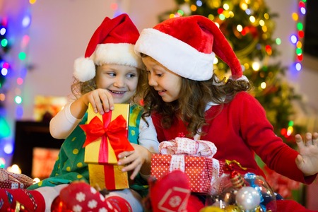 two little girls are opening presents around the Christmas treeの写真素材