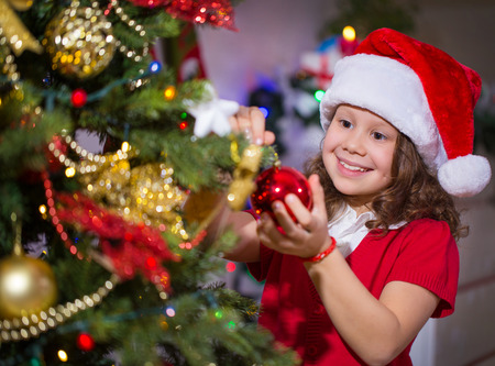 Little girl in Santa hat decorates a Christmas treeの写真素材