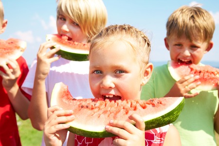 Children eating red watermelon on blue sky backgroundの写真素材