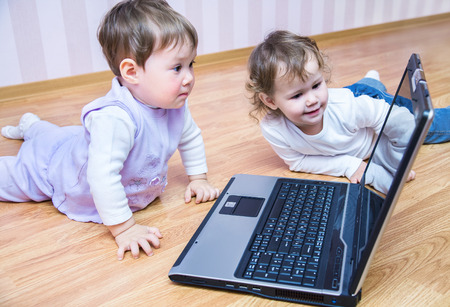 Kids playing with laptop on the floorの写真素材