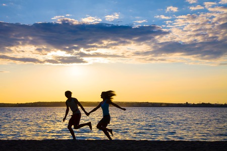 Young couple in love running at sunset on the beachの写真素材