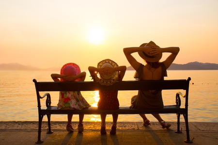 Family with children sitting on a bench on the seafront at sunset in the resortの写真素材