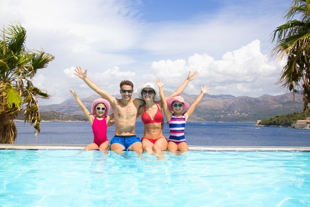 happy family with children sitting on the edge of the pool in a tropical seaside resort against the backdrop of the sea and palmsの写真素材