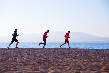 group of young people runs at the beach on beautiful summer sunsetの写真素材