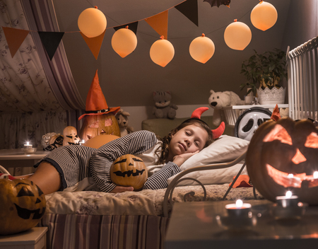 Little girl is sleeping in a children's bedroom decorated for Halloweenの写真素材